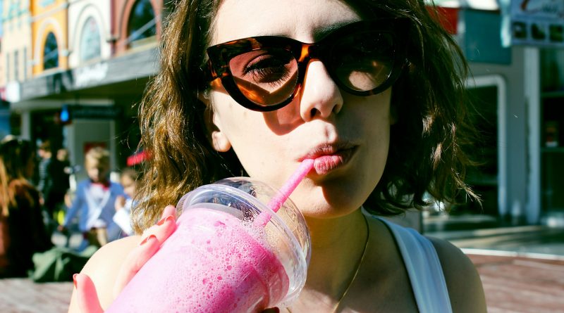 Junge Frau mit Sonnenbrille trinkt mit Strohhalm aus Becher