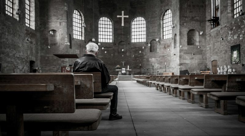 Älterer Mann sitzt alleine in einer Kirche.